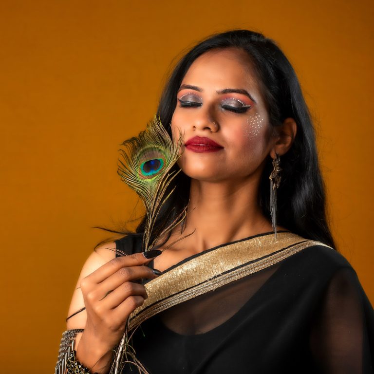 Beautiful Young Girl with bright makeup posing with peacock feathers on yellow background.